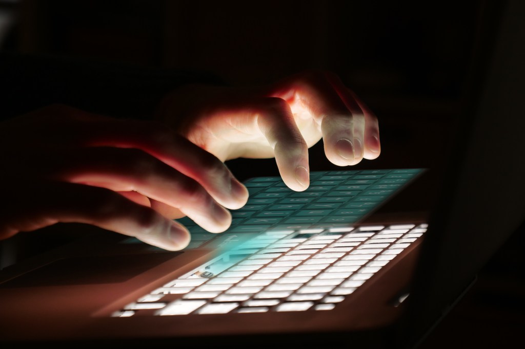 fingers typing on a hologram of a keyboard over a back-lit keyboard in the dark