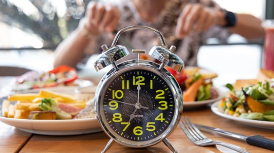Selective focus ofAlarm clock withyoung man eating a healthy food as Intermittent fasting, time-restricted eating-Diet breakfast image