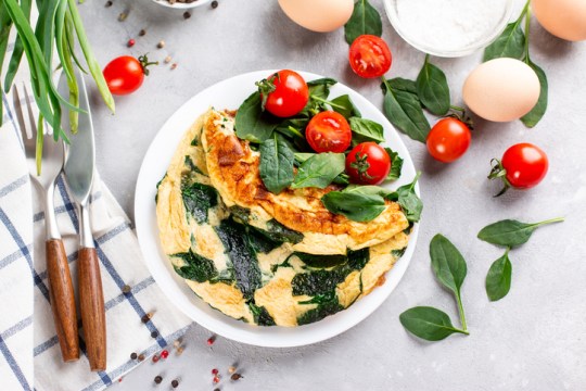 Delicious omelet with spinach, cheese and tomatoes on a white plate on a light slate or concrete background. Top view.